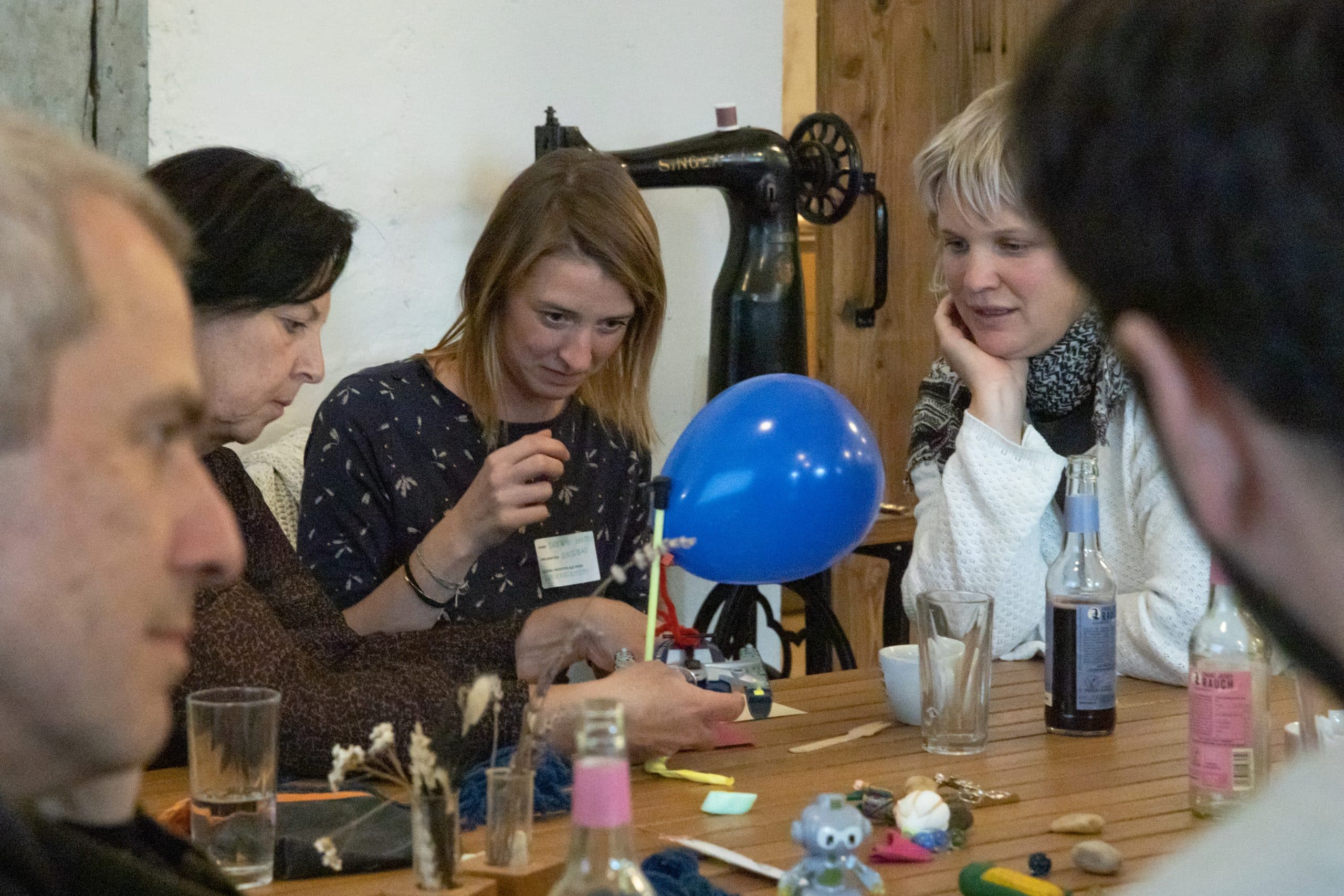 mehrere Personen sitzen um Tisch mit blauem Luftballon, bauen etwas, Ideen zur sozialen Innovation sammeln