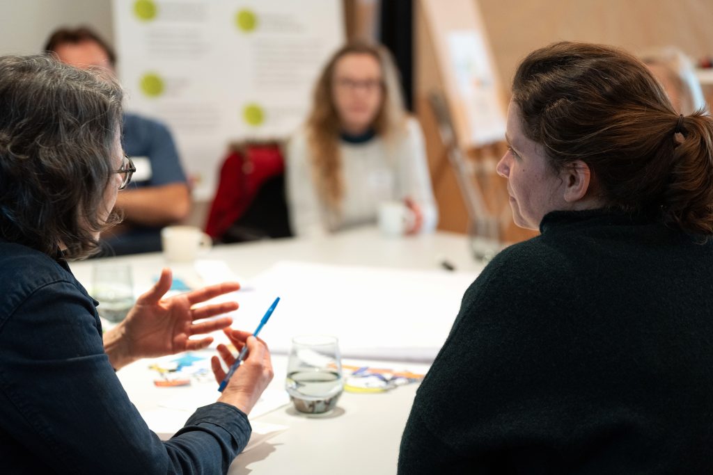 mehrere Personen sitzen um Tisch und diskutieren