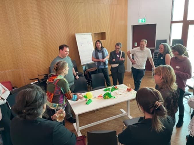 Teilhabe „zum Angreifen“ – Nachlese zum SI-plus-Nachmittag bei der ESF+ Jahrestagung 2026 - 14. April 2026 Personengruppe steht um einen Tisch mit bunten Materialien.