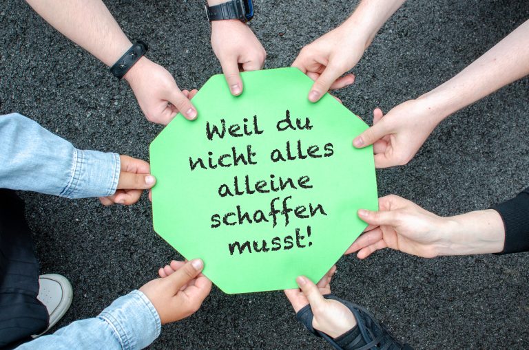Acht Hände halten einen bunten Zettel mit der Aufschrift "Weil du nicht alles alleine schaffen musst!"